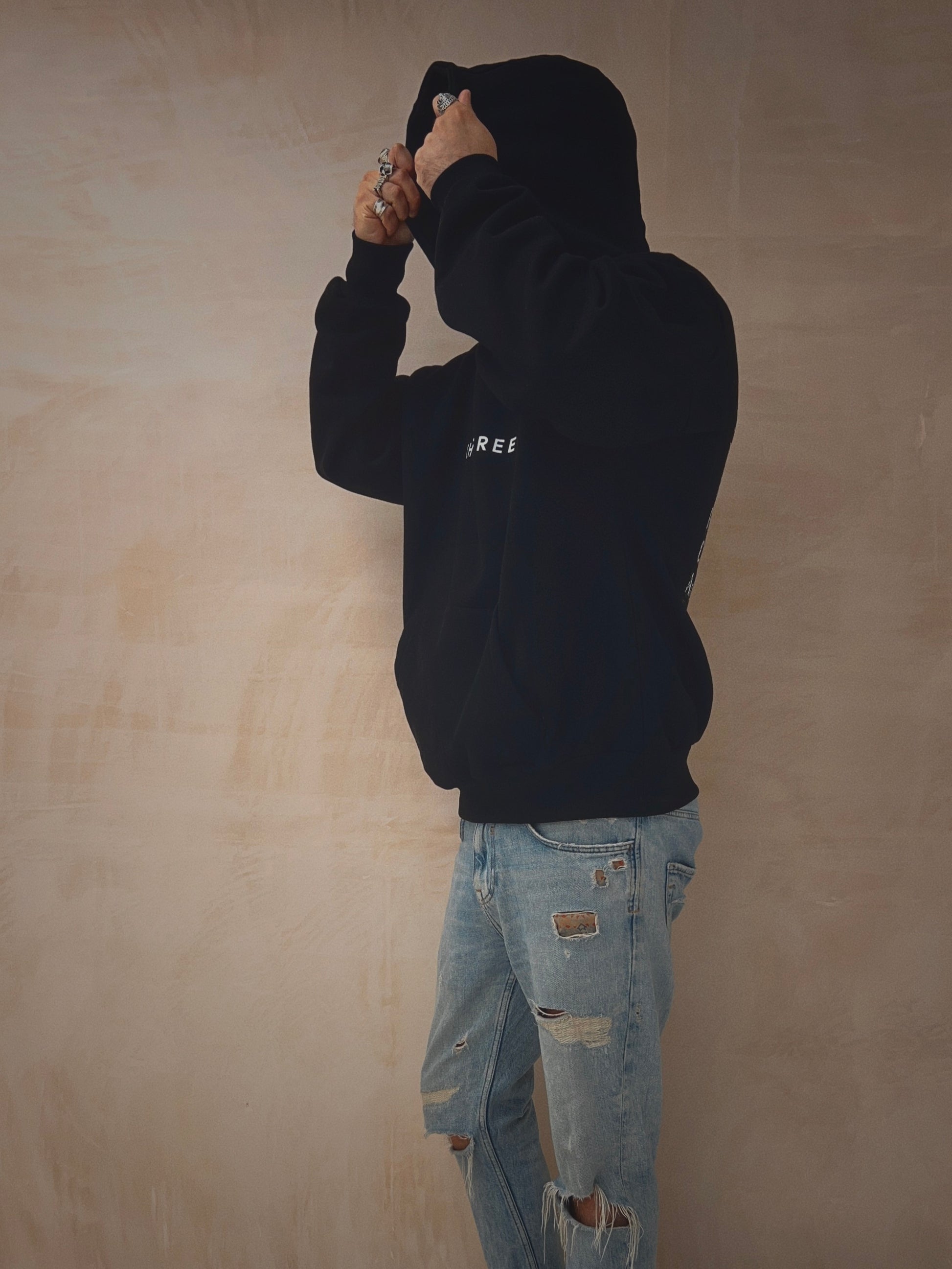 Male wearing a black oversized hoodie with slogan on